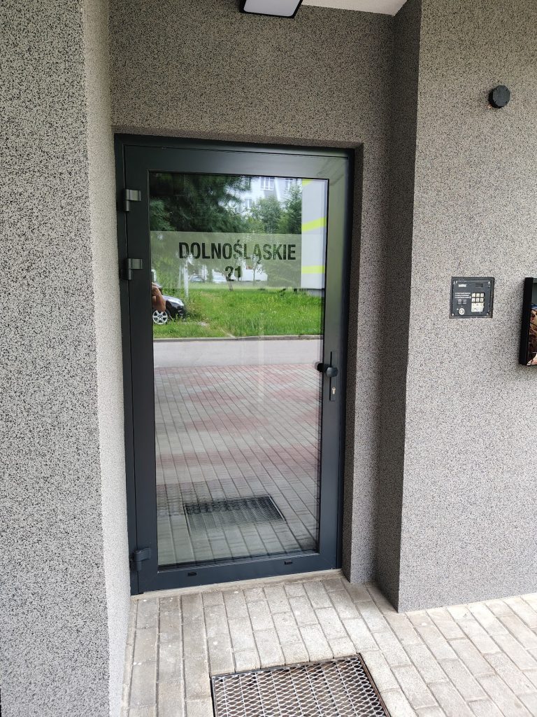 Antracytowe drzwi aluminiowe do budynku wielorodzinnego z panelem domofonowym